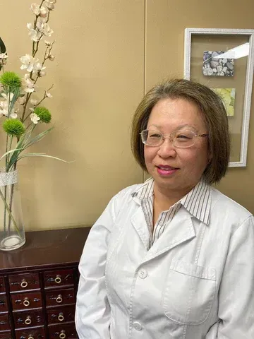 Amy Wang standing in front of a vase of flowers in a white lab coat and glasses