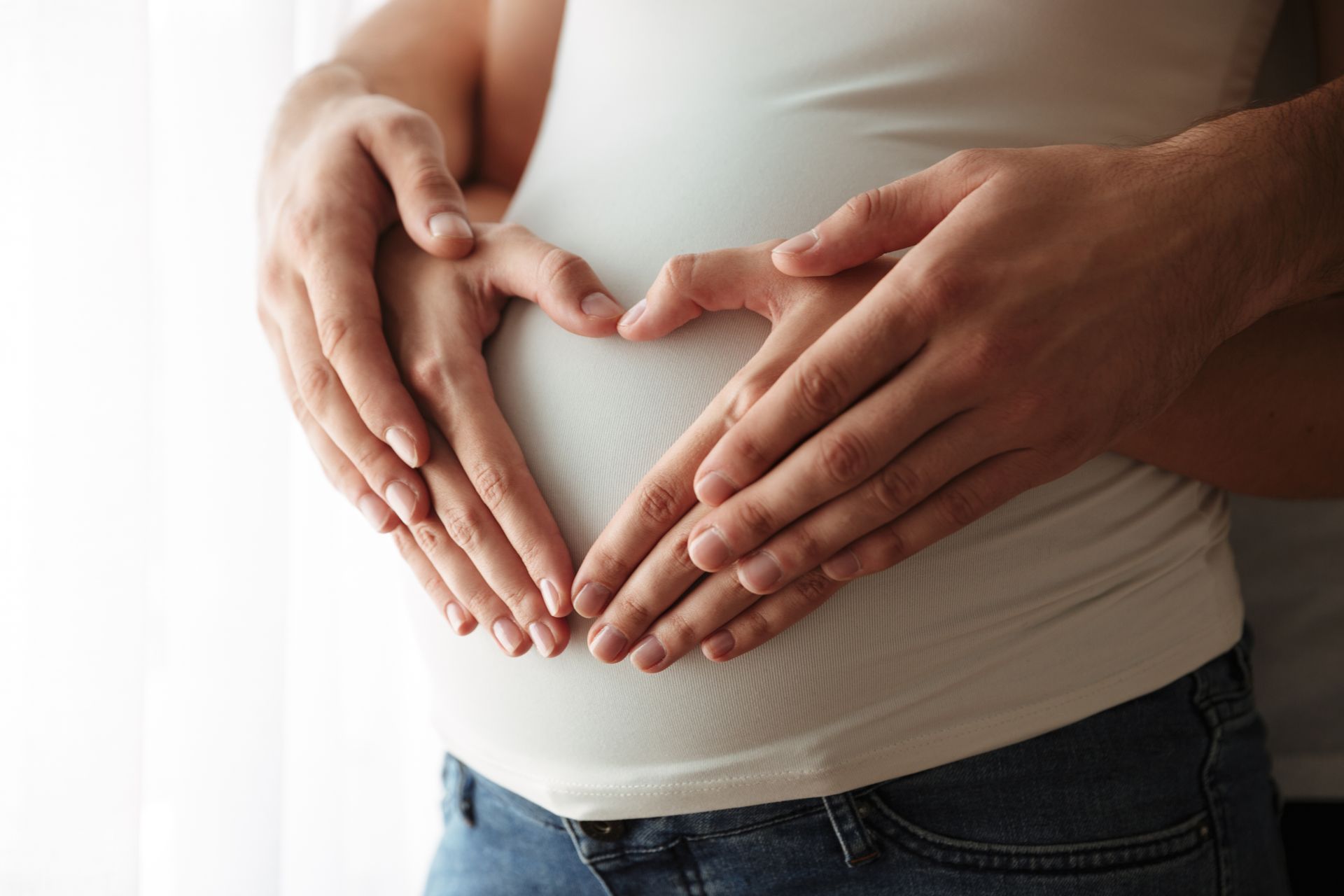 A man and a woman making a heart shape with their hands on a pregnant belly