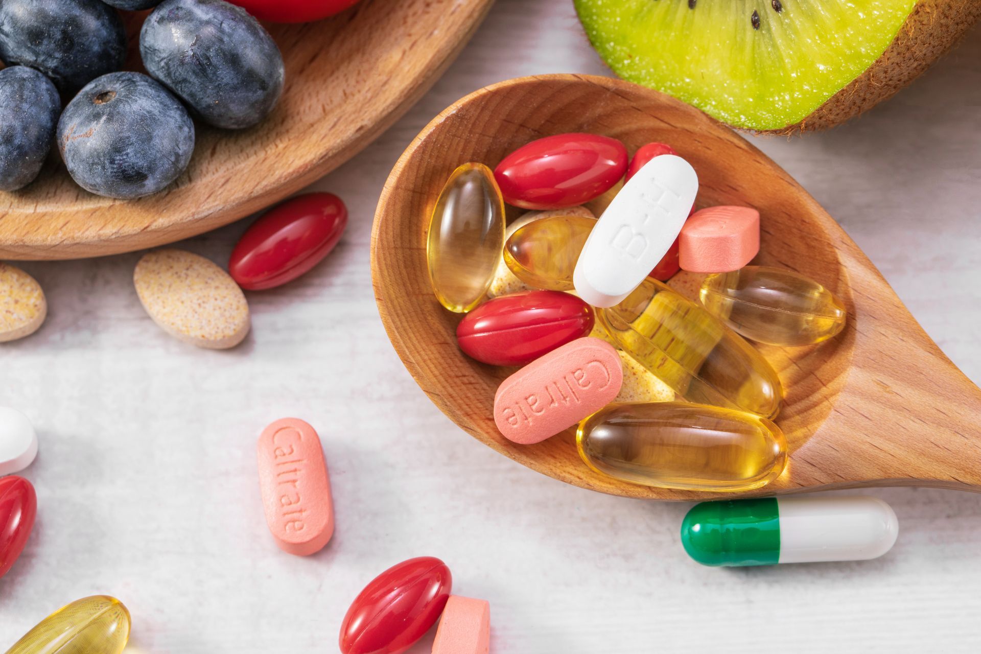 A wooden spoon filled with different colored pills and fresh fruits