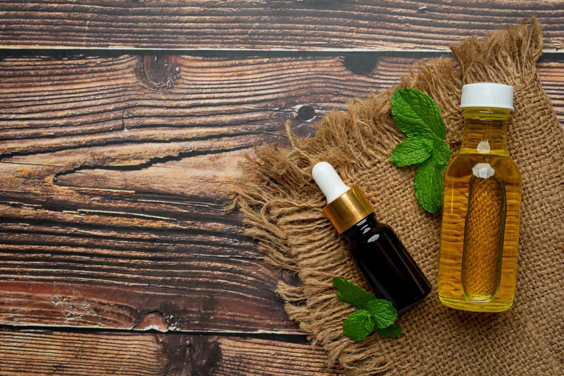 Two bottles of essential oil with mint leaves on a wooden table