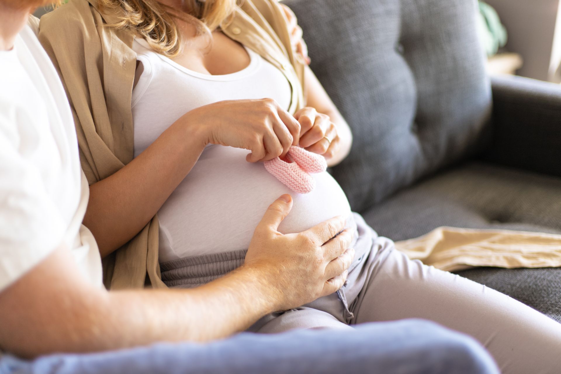 A pregnant woman holds pink baby shoes on her belly