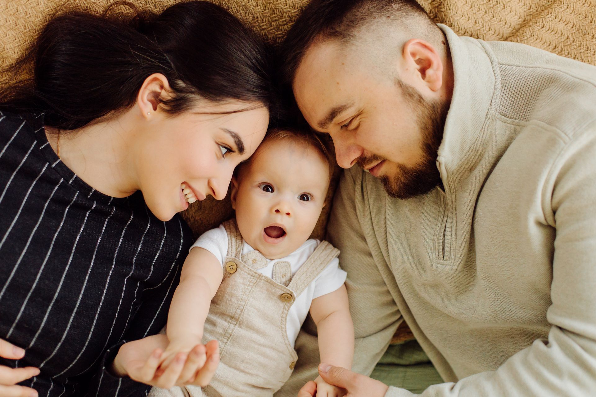 A man and woman laying on a blanket with a baby