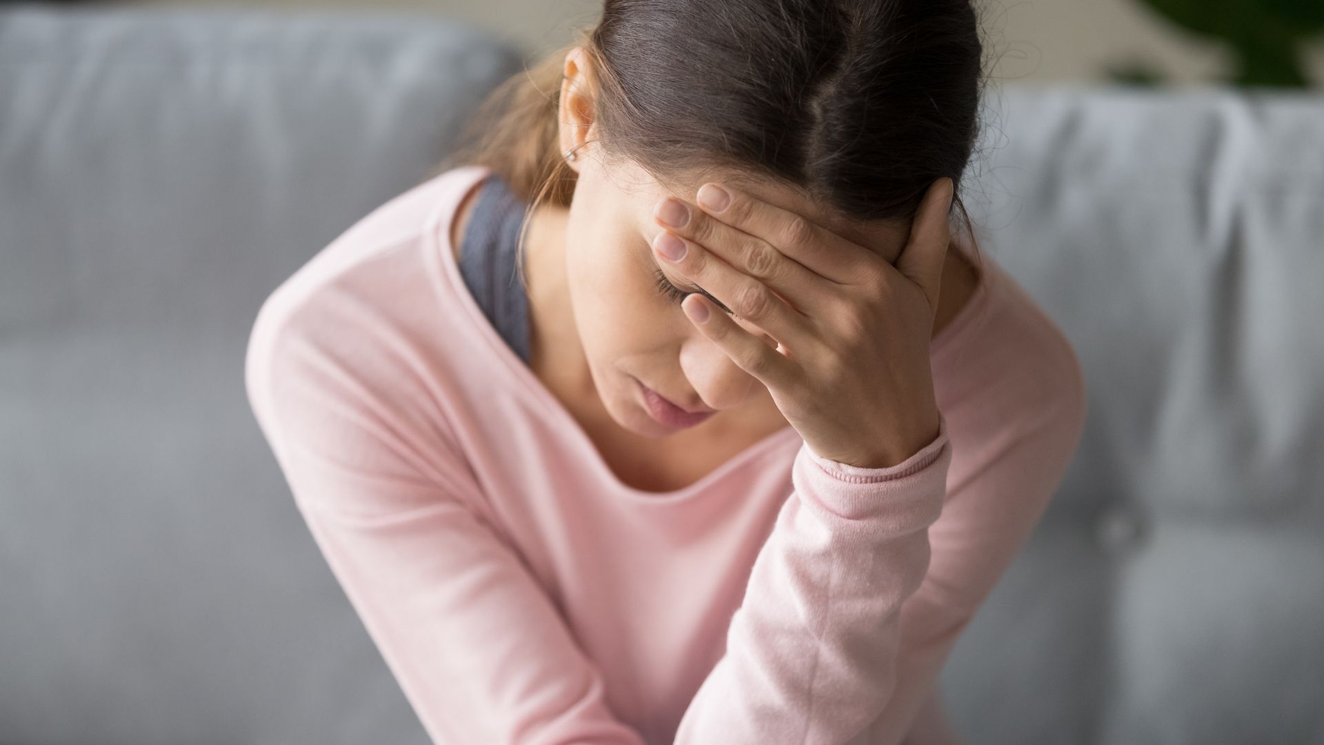 A woman in a pink shirt is covering her face with her hand