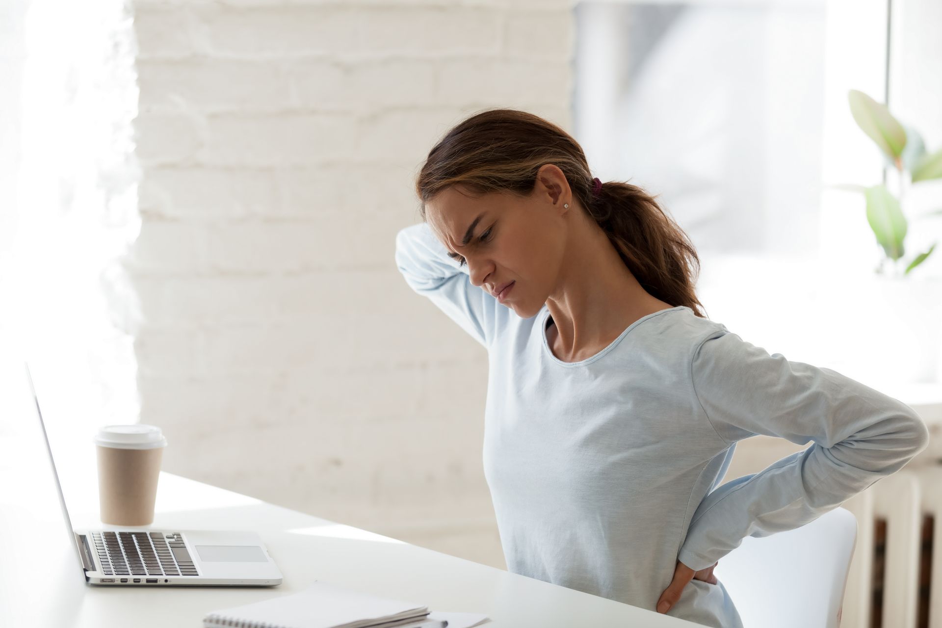 A woman holds her neck in pain while sitting in front of a laptop