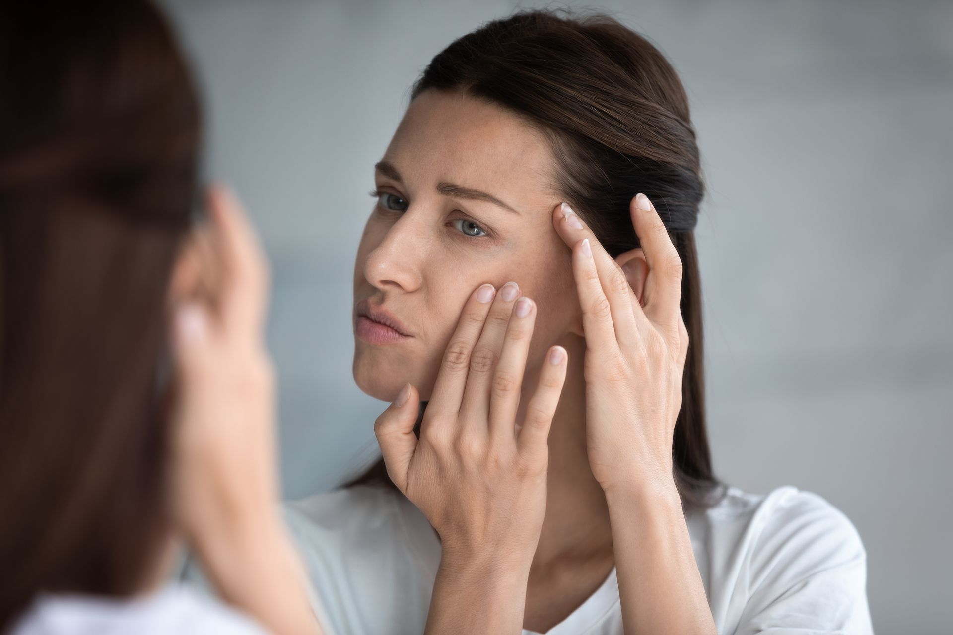 A woman is looking at her face in a mirror