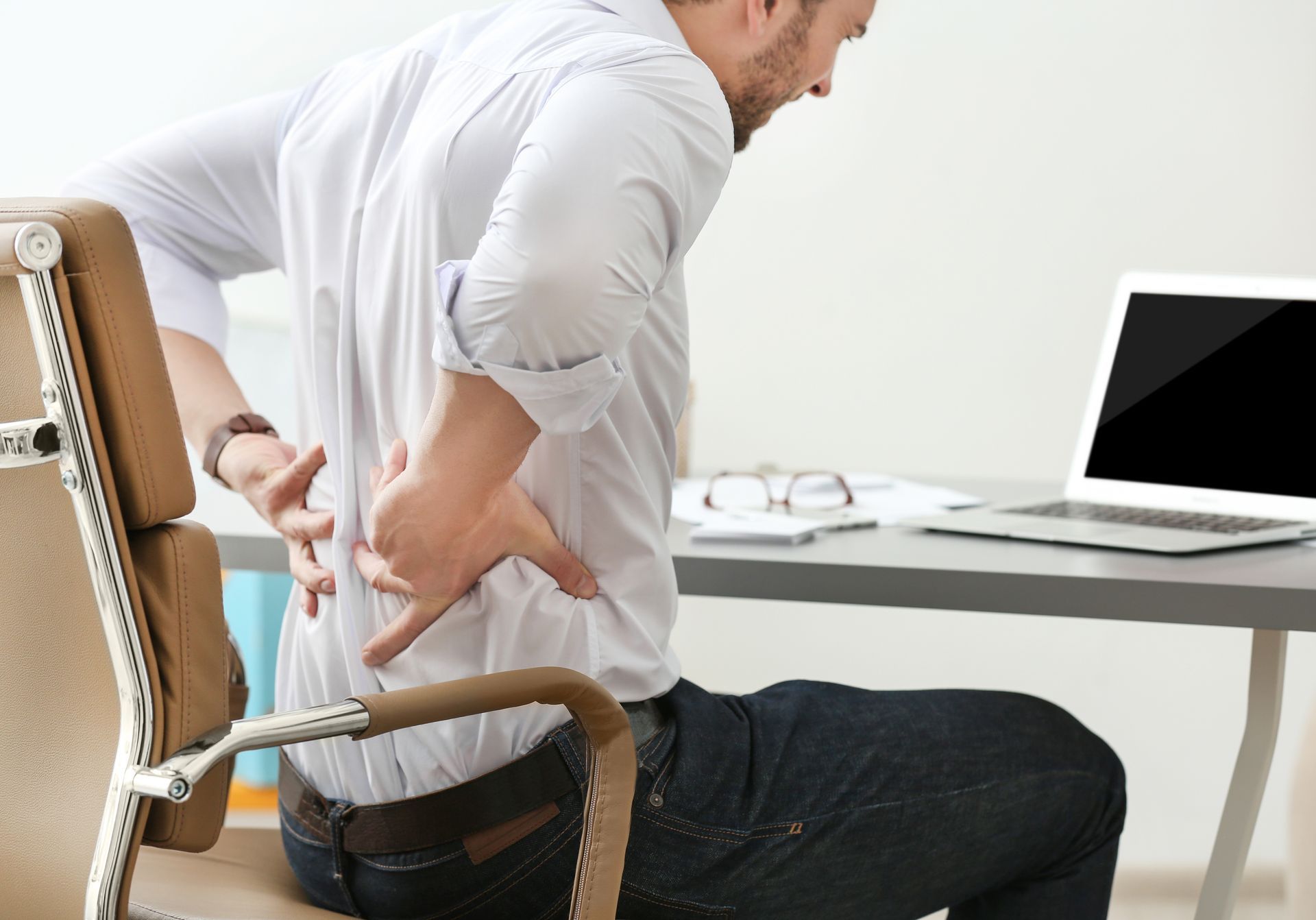 A man sits in an office chair holding his back in pain